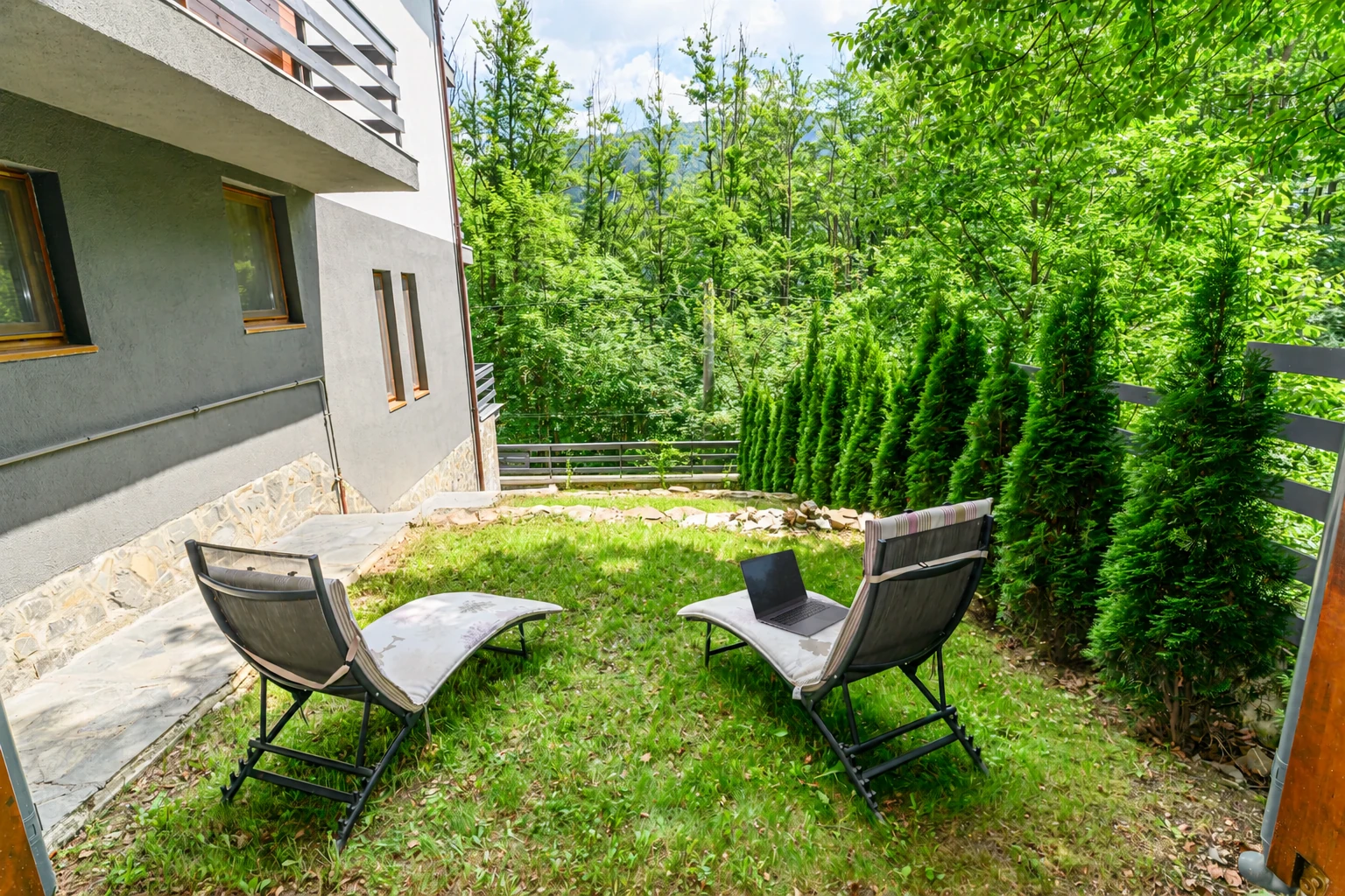 A laptop on a lounger in the Hublou Home garden, with the forest behind
